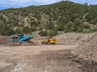 two yellow bulldozers work on sand and gravel in a mountain valley while another one looks at it