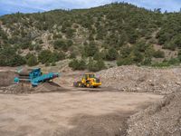 two yellow bulldozers work on sand and gravel in a mountain valley while another one looks at it