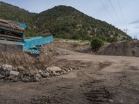 two yellow bulldozers work on sand and gravel in a mountain valley while another one looks at it