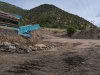 two yellow bulldozers work on sand and gravel in a mountain valley while another one looks at it