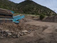 two yellow bulldozers work on sand and gravel in a mountain valley while another one looks at it