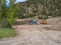 two yellow bulldozers work on sand and gravel in a mountain valley while another one looks at it