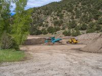 two yellow bulldozers work on sand and gravel in a mountain valley while another one looks at it