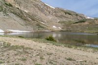 a horse is grazing near a lake in a mountain area, surrounded by mountains and snow