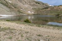 a horse is grazing near a lake in a mountain area, surrounded by mountains and snow