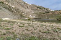 a horse is grazing near a lake in a mountain area, surrounded by mountains and snow