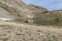 a horse is grazing near a lake in a mountain area, surrounded by mountains and snow