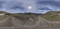 a cloudy sky appears to be shown as seen through the camera lens of a dirt road with trees and mountains