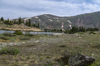 some snow and rocks in the middle of a meadow with mountains in the background and two water buffalos