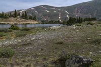 some snow and rocks in the middle of a meadow with mountains in the background and two water buffalos