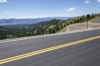 a motor cycle on an asphalt road looking out to the mountains and valley below it