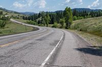 a lone motorcycle travels along a curvy road in the country mountains and meadows