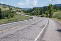 a lone motorcycle travels along a curvy road in the country mountains and meadows