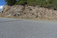 a small motorcycle parked on a road beside a cliff with trees and bushes in the background