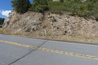 a small motorcycle parked on a road beside a cliff with trees and bushes in the background