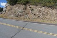 a small motorcycle parked on a road beside a cliff with trees and bushes in the background