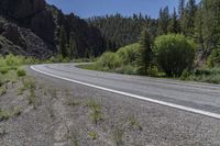 a motorcycle driving down a paved highway in front of a canyon side area with trees