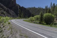 a motorcycle driving down a paved highway in front of a canyon side area with trees