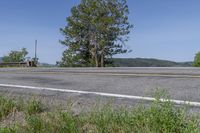 an asphalt road with grass and weeds by the side of the road and a fence in the distance