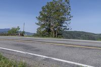 an asphalt road with grass and weeds by the side of the road and a fence in the distance