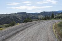 a long gravel road running up the side of a mountain in the background is mountains