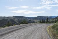 a long gravel road running up the side of a mountain in the background is mountains