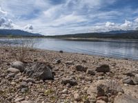 a lake with rocks on the shore and mountains in the background along side it and snow capped hills