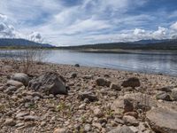 a lake with rocks on the shore and mountains in the background along side it and snow capped hills