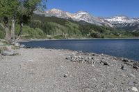 a view of a beach with mountains in the background at a lake, surrounded by rocks, and rocks