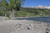 a view of a beach with mountains in the background at a lake, surrounded by rocks, and rocks