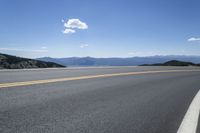 an empty asphalt highway with yellow lines down the middle of it next to mountains and blue skies