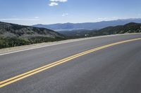 an empty asphalt highway with yellow lines down the middle of it next to mountains and blue skies