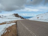 an empty road with snow and mountains in the back ground under cloudy skies on a sunny day