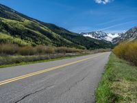 the road is paved with yellow markings and has a snowy mountain range in the background