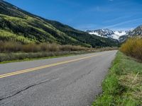 the road is paved with yellow markings and has a snowy mountain range in the background