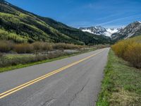 the road is paved with yellow markings and has a snowy mountain range in the background