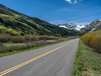 the road is paved with yellow markings and has a snowy mountain range in the background