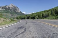 the motorcycle is parked on the empty street next to the mountains, and there's a yellow and blue sign pointing up for the bikers