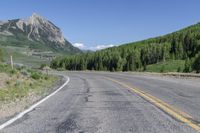 the motorcycle is parked on the empty street next to the mountains, and there's a yellow and blue sign pointing up for the bikers