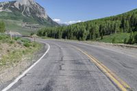 the motorcycle is parked on the empty street next to the mountains, and there's a yellow and blue sign pointing up for the bikers