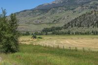 a field with some green tractor in the distance next to hills and grass with trees