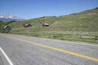 a road in front of a mountain with barn buildings on it and snow capped mountains