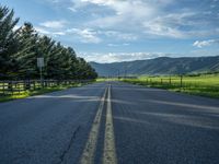 a empty road that goes through a grassy area with mountains in the background as well as trees