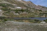 a lake and a mountain, with green vegetation on the side of it with snow covered mountains