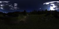 the moon shines brightly behind the clouds in the night sky above a meadow with trees on a hillside below