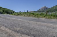 the road has very little gravel along side it and trees line around the mountains in the distance