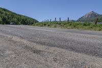 the road has very little gravel along side it and trees line around the mountains in the distance