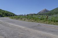 the road has very little gravel along side it and trees line around the mountains in the distance