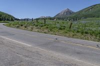 the road has very little gravel along side it and trees line around the mountains in the distance