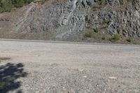 an empty road in the middle of a mountain area near a cliff, with rocks and grass on both sides